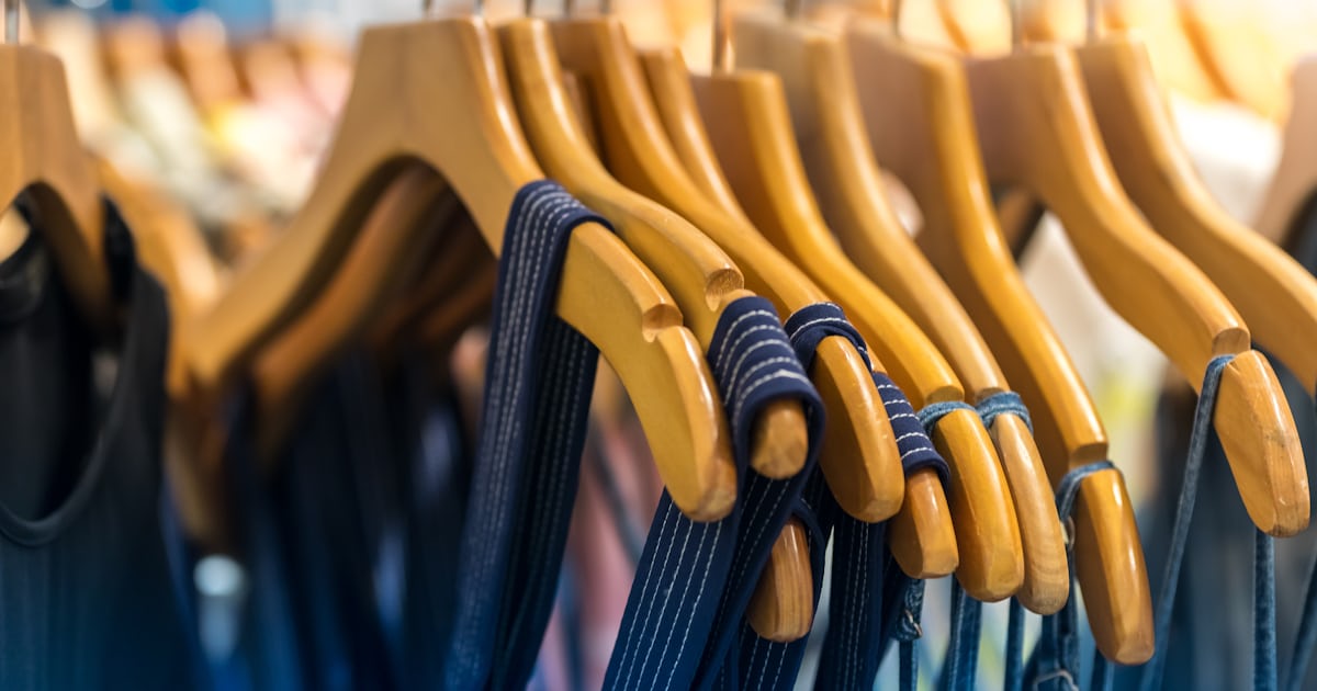 Peças de roupa penduradas em cabides de madeira em uma arara de loja, vistas de perto