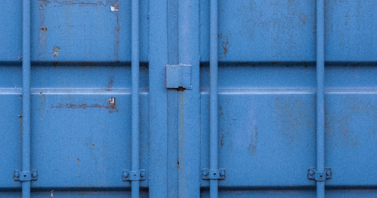 Detalhe das portas fechadas de um container de carga azul, com as barras verticais de travamento e as dobradiças de metal