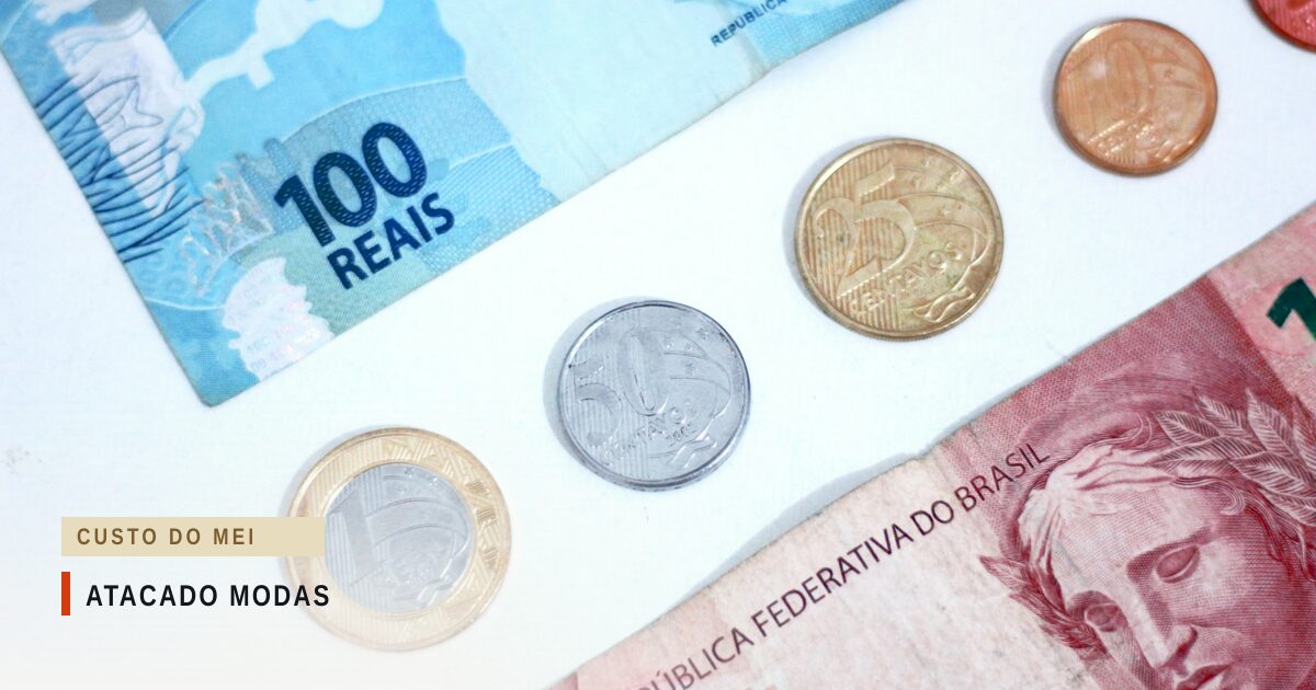 Cédula de cem reais no alto e cédula avermelhada com a inscrição República Federativa do Brasil embaixo, com quatro moedas de real entre elas, sobre fundo branco, vistas de cima