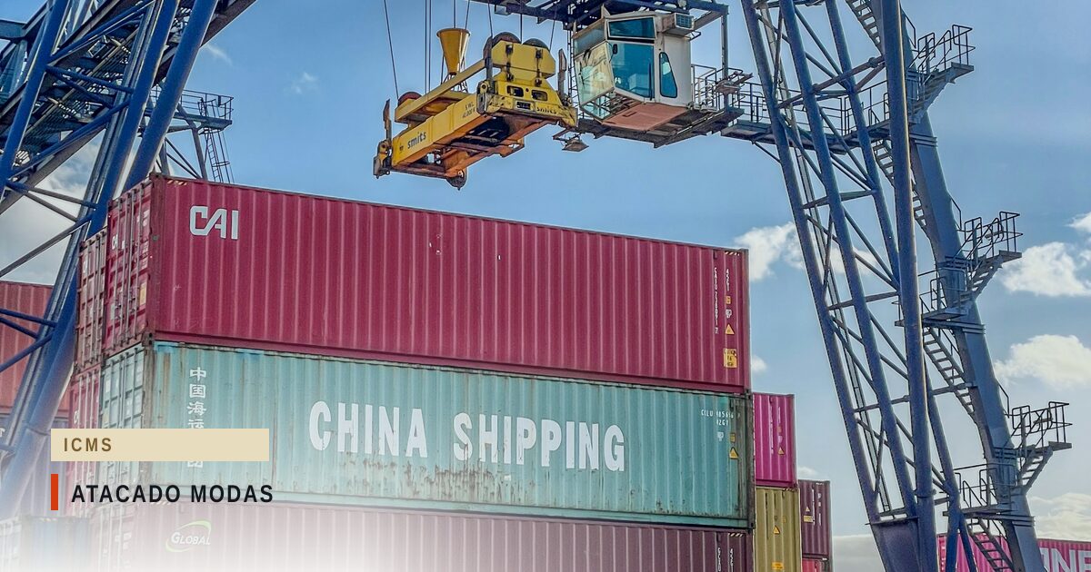 Pórtico de porto içando um contêiner vermelho sobre pilhas de contêineres, um deles com a inscrição China Shipping, sob céu azul