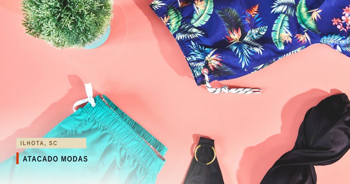 Peças de moda praia sobre fundo rosa: um short de banho verde-água, um short estampado com folhagens tropicais em azul e partes de biquíni pretas, uma delas com argola dourada