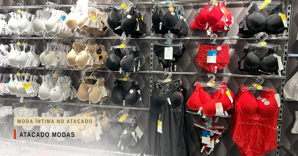Parede de loja com fileiras de sutiãs brancos, bege, pretos e vermelhos em ganchos, um body de renda vermelho e uma camisola preta