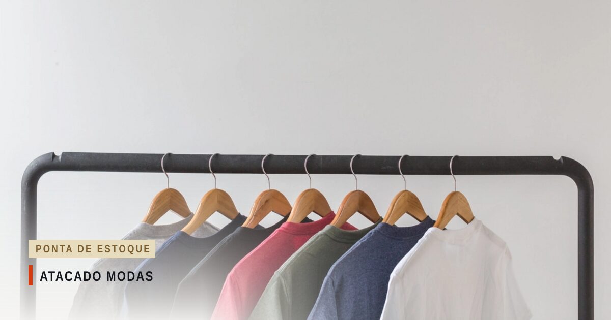 Camisetas de sete cores penduradas em cabides de madeira numa arara de metal preto, diante de uma parede branca