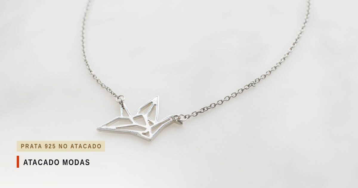 Colar de corrente prateada com pingente vazado em forma de tsuru, a garça do origami, sobre mármore branco